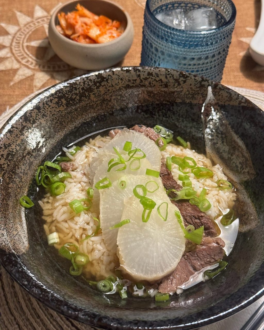 Bowl of clear beef and radish soup over rice with sliced brisket, daikon and green onion, kimchi on the side