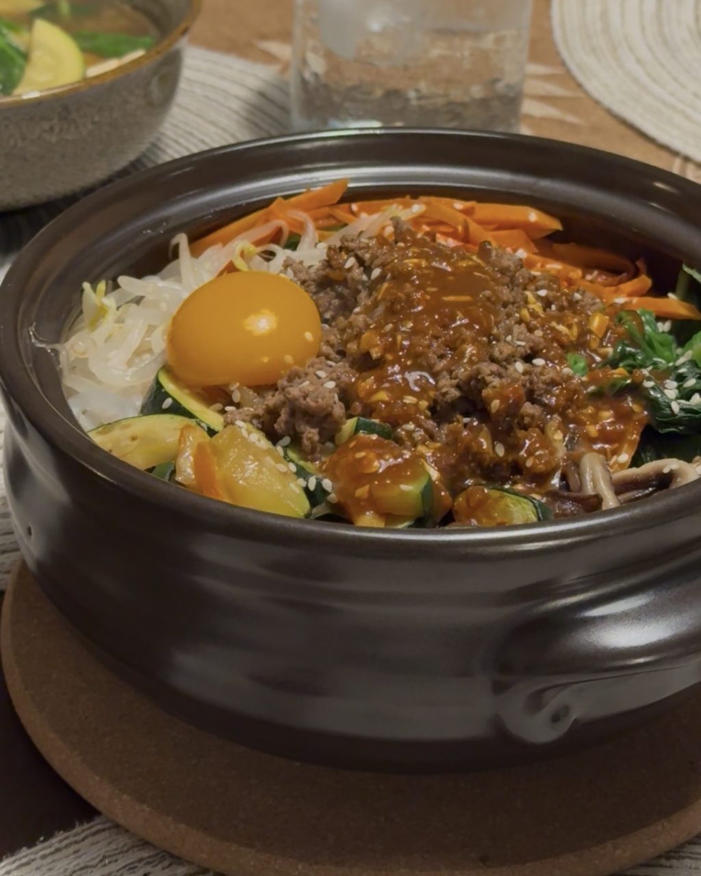 Bibimbap in a black stone bowl with carrots, zucchini, spinach, bean sprouts, gochujang beef and a raw egg yolk