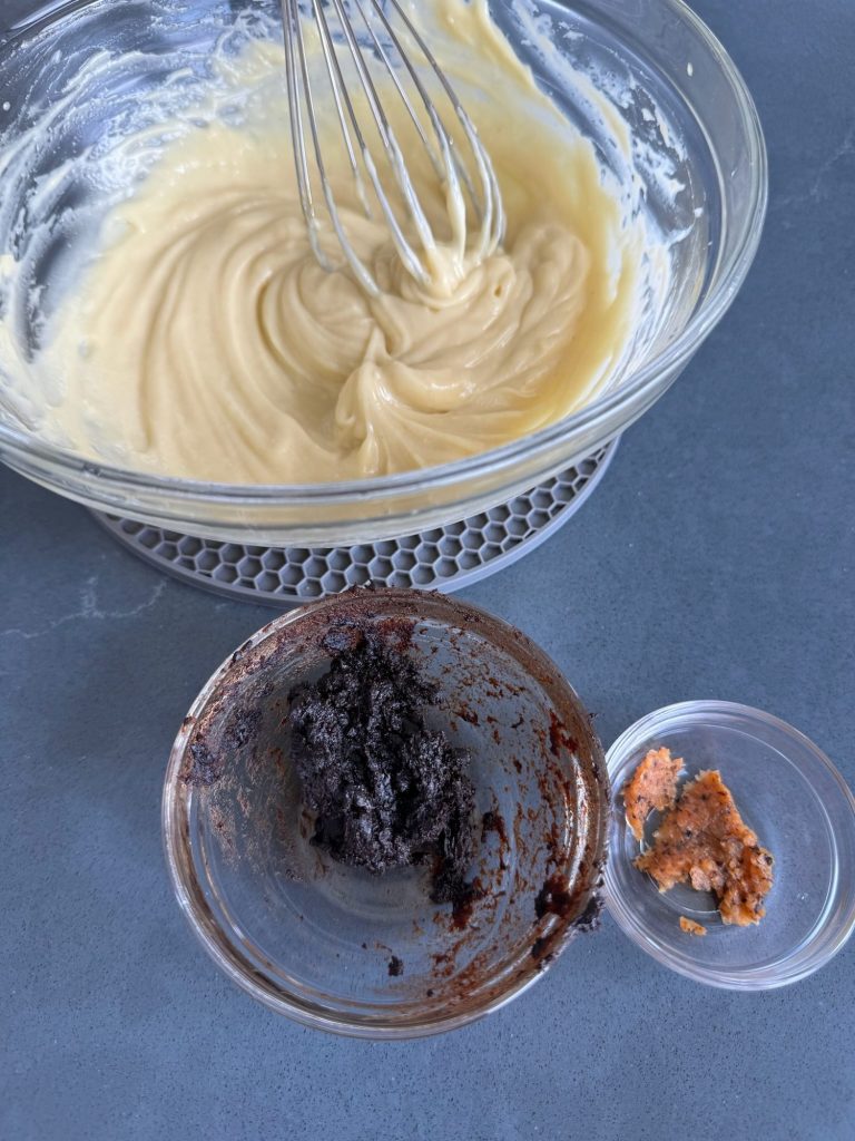 Whisked aioli base in a glass bowl with small dishes of mashed black garlic and minced roasted habanero