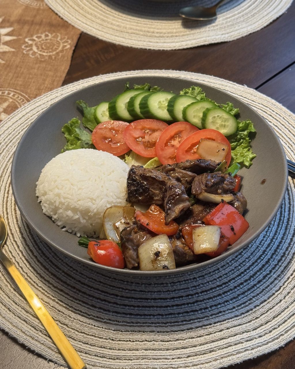 Plate of seared beef cubes with onions and bell peppers, served with rice, tomatoes, cucumbers and lettuce