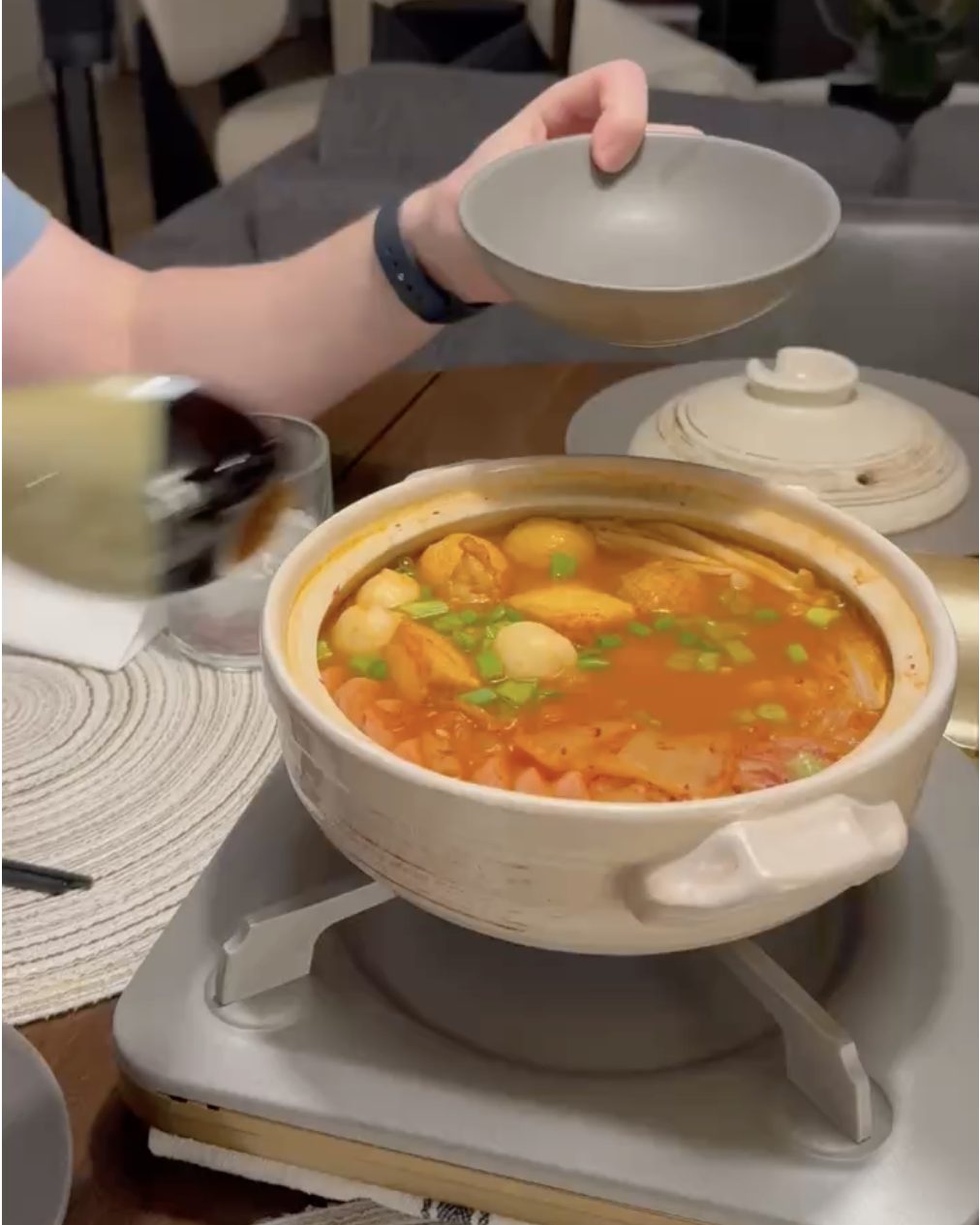 Clay pot of bubbling Korean army stew with fish cakes, kimchi and green onions in a spicy red broth on a tabletop burner