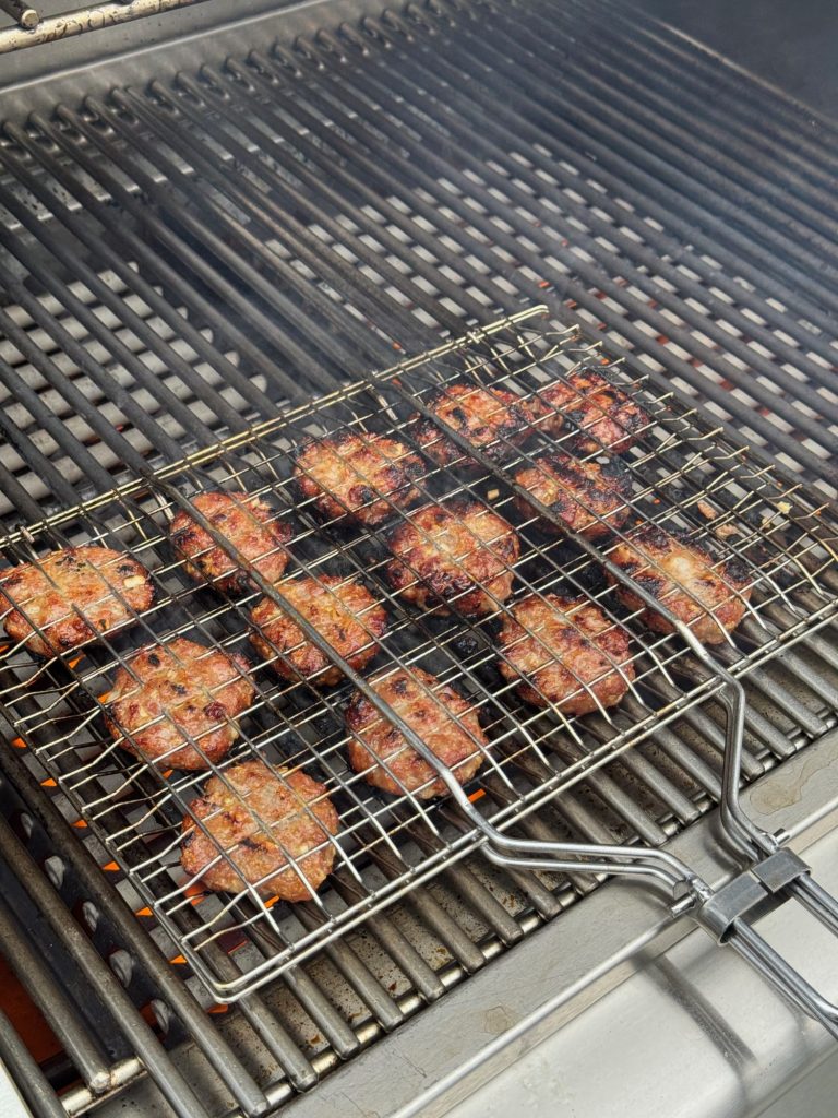 Lemongrass pork patties charring in a wire grill basket on a gas grill