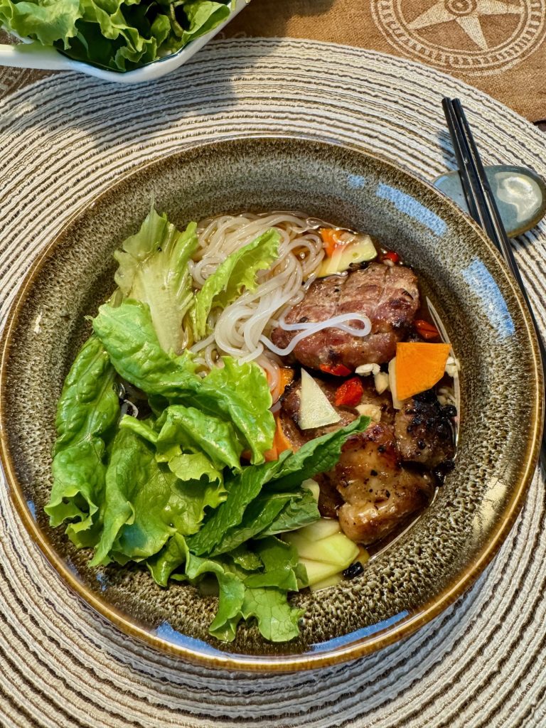 A bowl of bún chả with vermicelli, lettuce, grilled pork and patties dipped into the sauce with pickled papaya and carrot