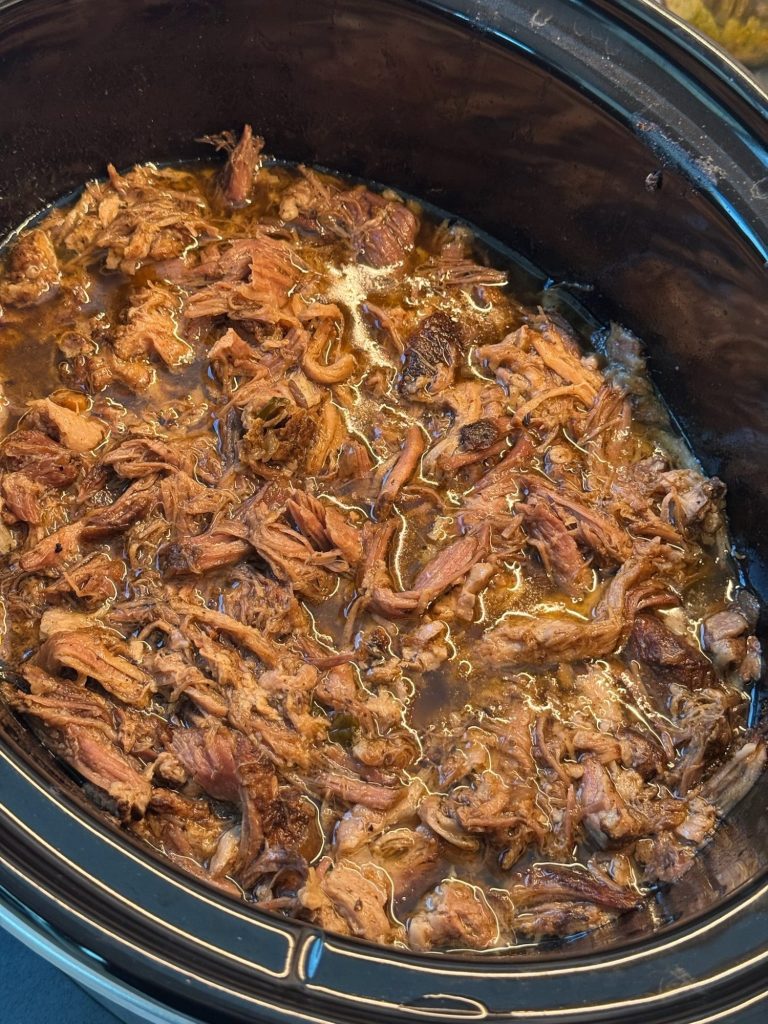 Shredded pork carnitas in its cooking juices in a slow cooker