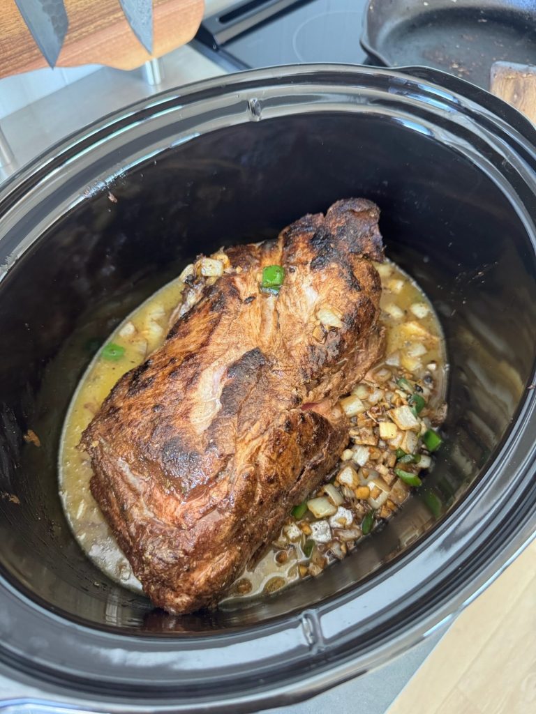 Seared pork shoulder in a slow cooker with broth, onion, garlic and jalapeño