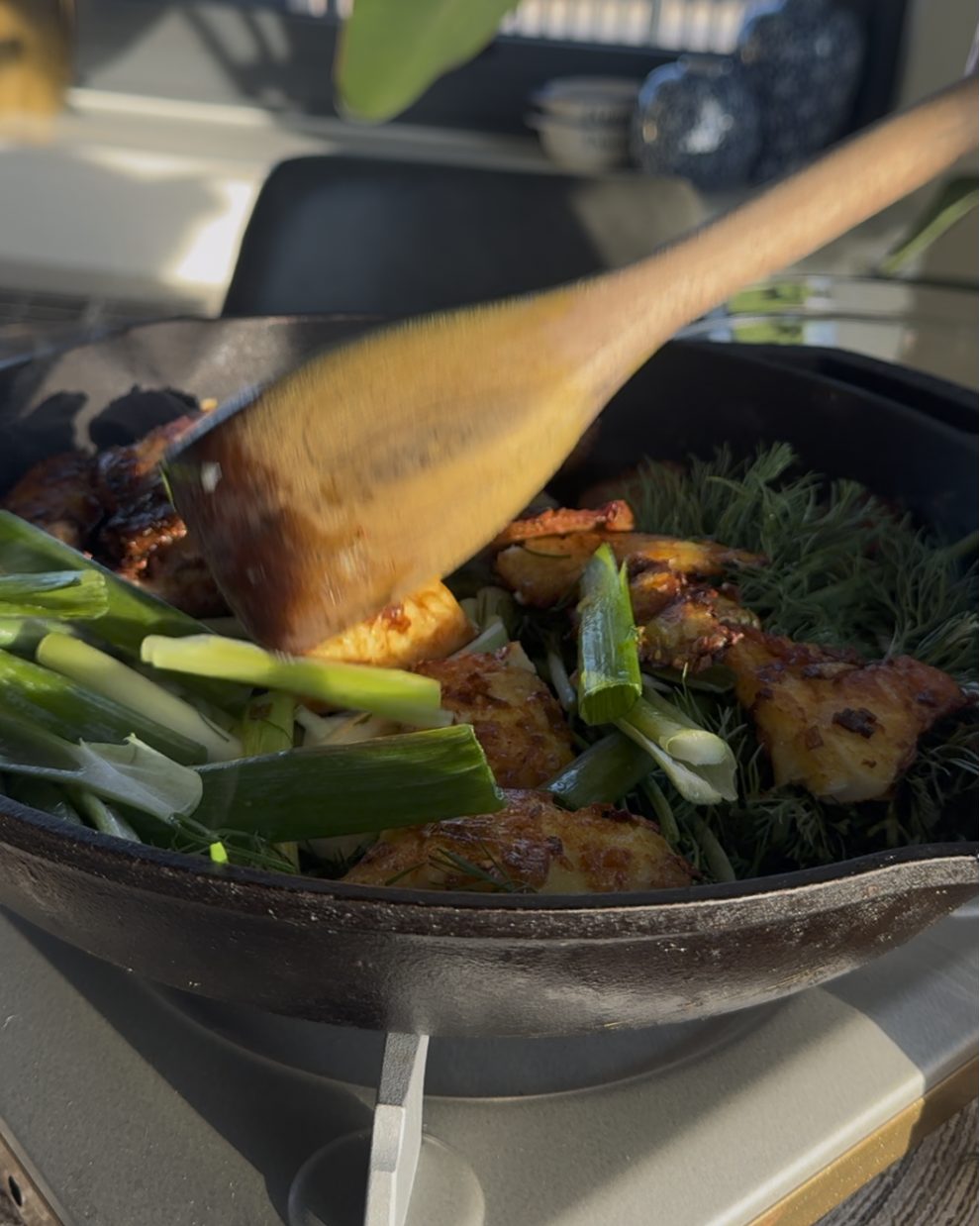 Turmeric fried fish tossed with dill and green onions in a cast iron skillet on a tabletop burner