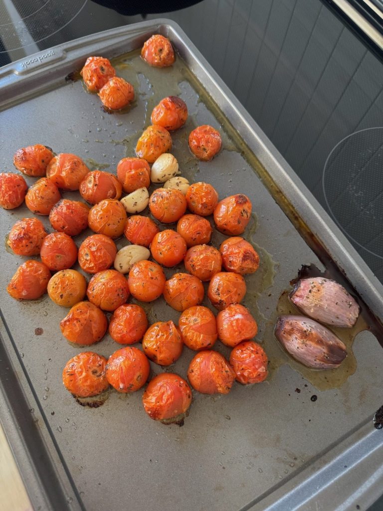 Blistered roasted cherry tomatoes, garlic cloves and shallot halves on a baking sheet