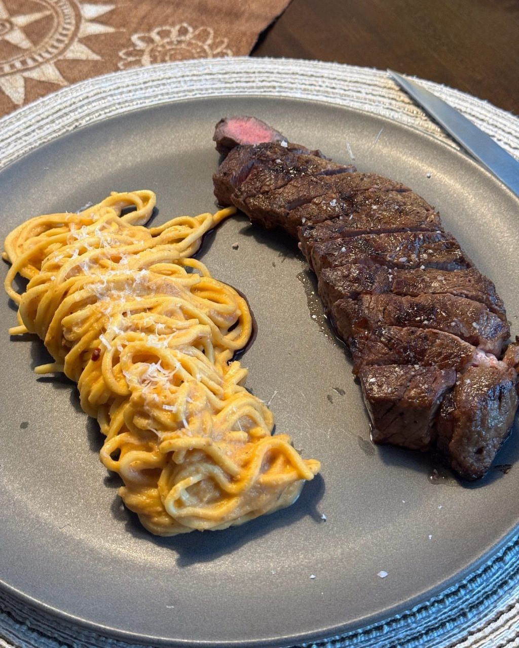 Twirl of creamy roasted cherry tomato spaghetti topped with parmesan, next to sliced seared steak on a gray plate