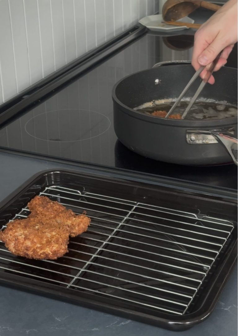A fried panko-crusted chicken thigh draining on a wire rack while another piece fries in a pan of oil