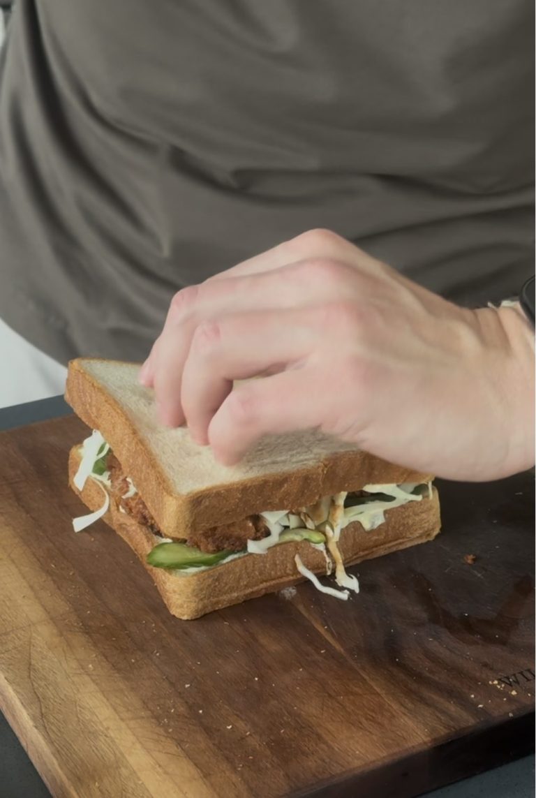 Pressing the top slice of bread onto a katsu sando layered with chicken, cucumber and shredded cabbage