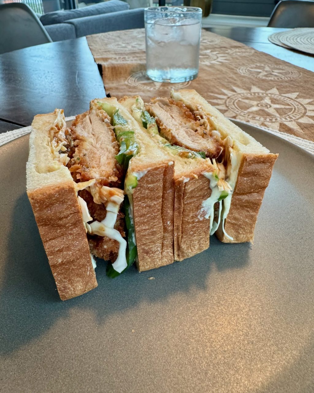 Chicken katsu sando cut in half on a gray plate, showing crispy panko chicken, shredded cabbage, cucumber and sauce between thick white bread