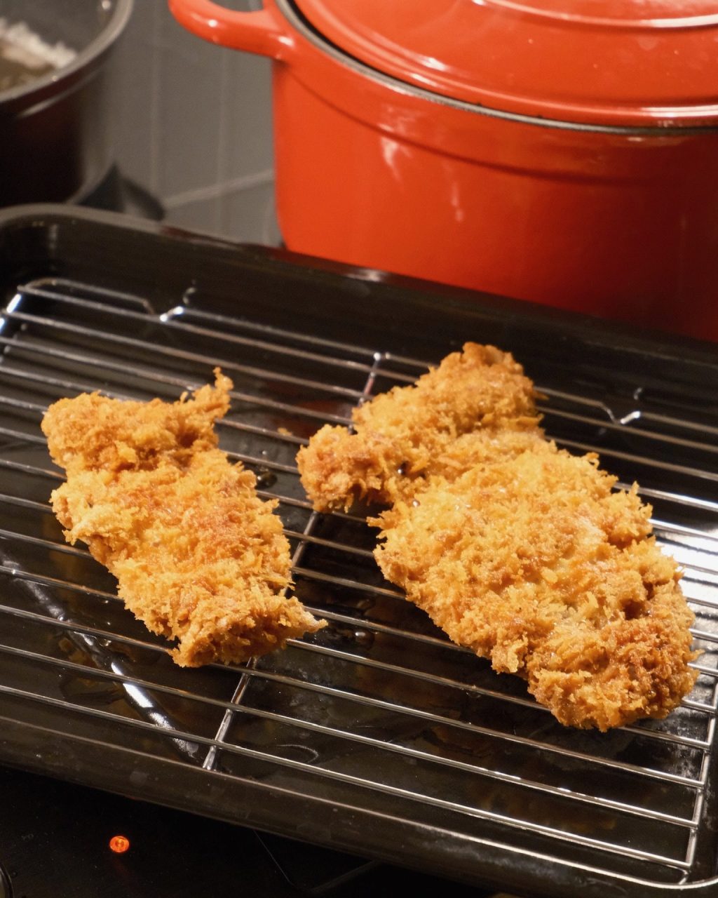 Two golden panko-fried chicken katsu cutlets draining on a wire rack