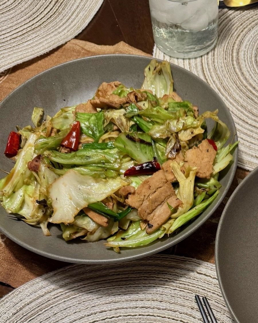 Chinese cabbage stir fry with seared pork belly, scallions and dried red chilies on a gray plate