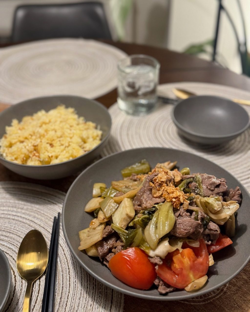 Plate of beef stir-fried with pickled mustard greens and tomatoes, with a bowl of golden fried rice and table settings