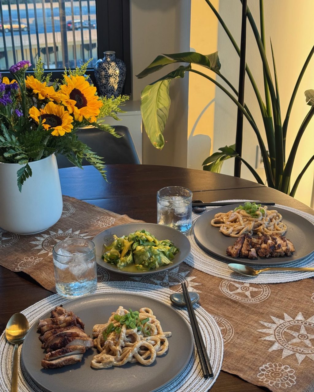 Dinner table set with plates of creamy miso udon topped with green onion, sliced grilled chicken and a cucumber salad