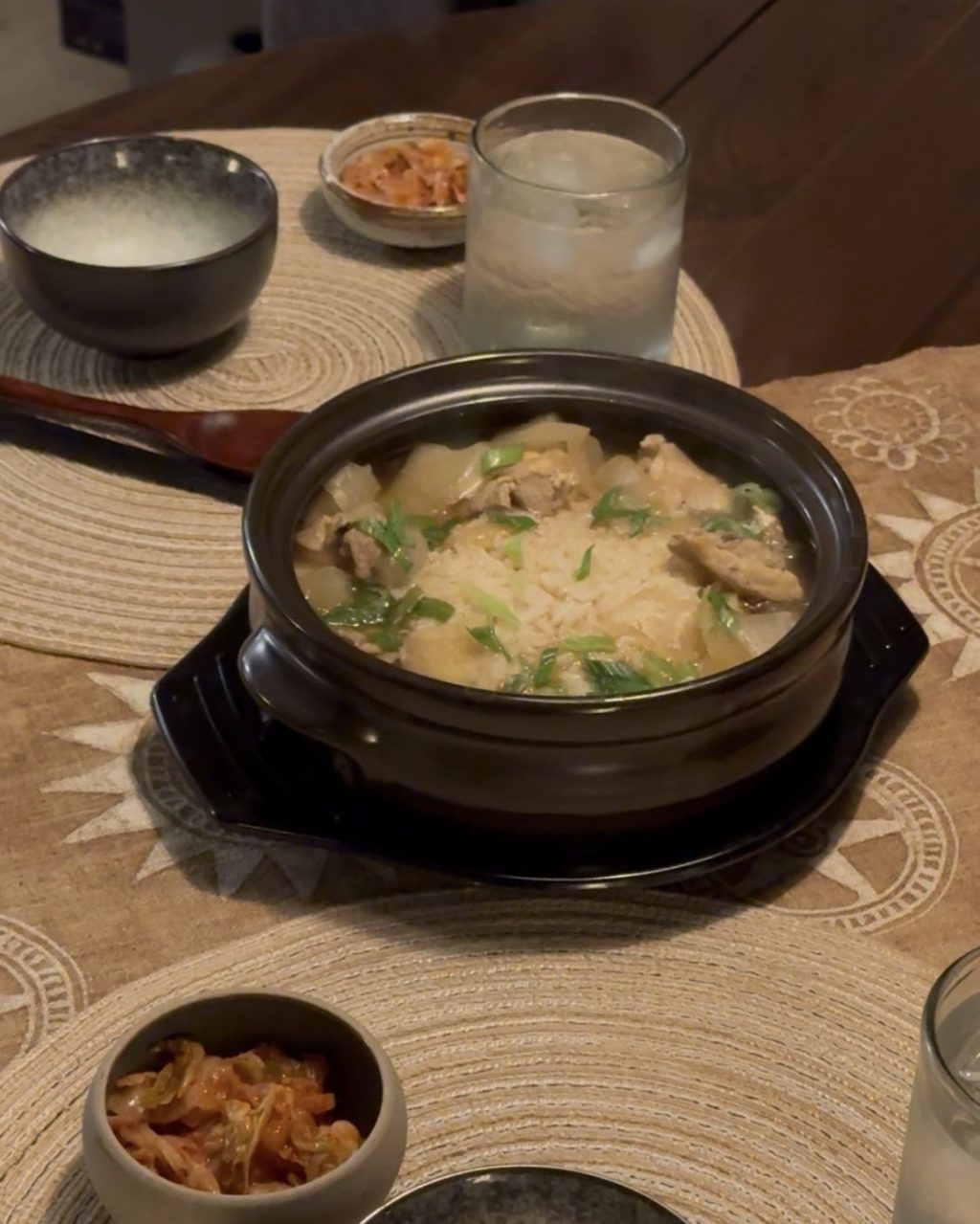 Korean chicken soup in a black clay pot with chicken, radish, rice and sliced green onions