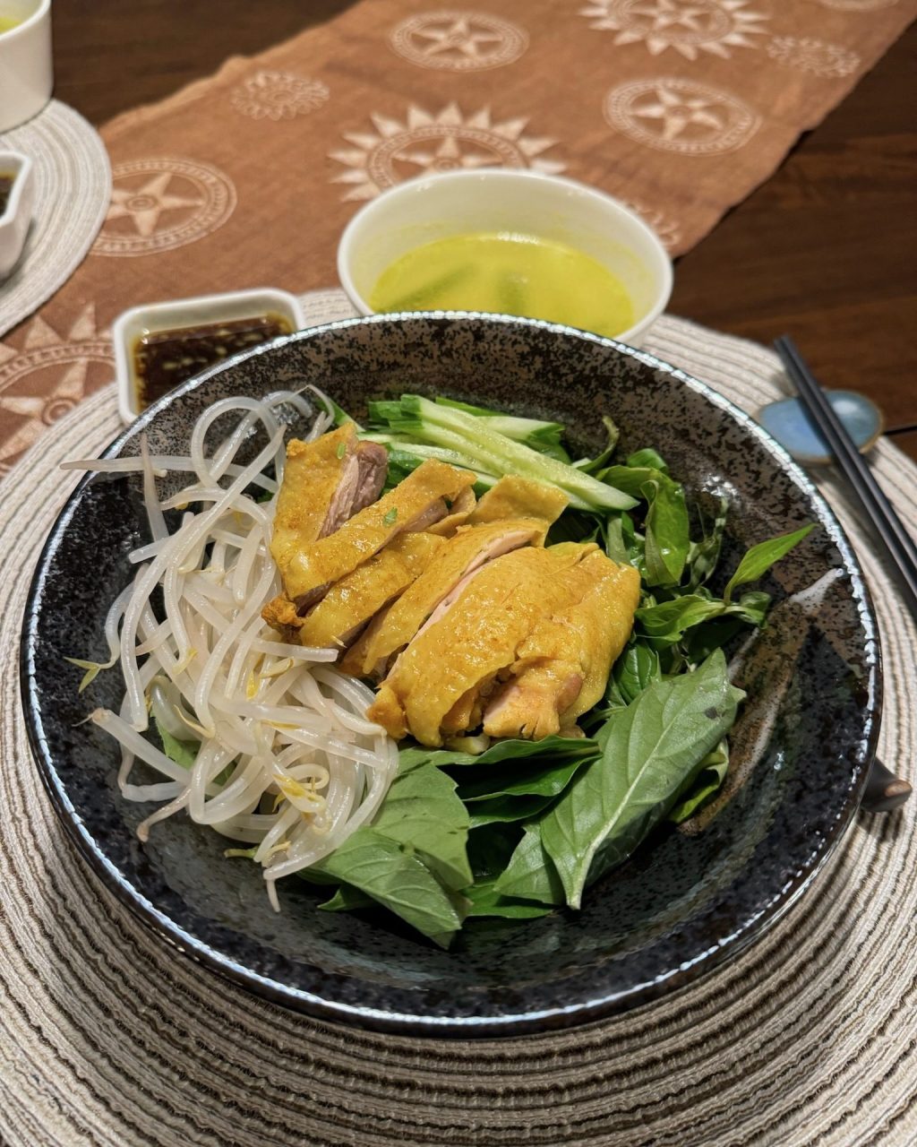 Bowl of dry pho noodles with turmeric poached chicken, bean sprouts, cucumber and fresh herbs, with dipping sauce and broth on the side