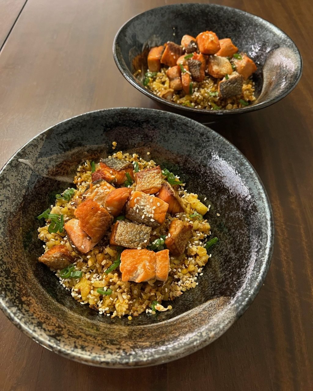 Bowl of golden egg fried rice topped with crispy cubes of salmon, scallions and sesame seeds