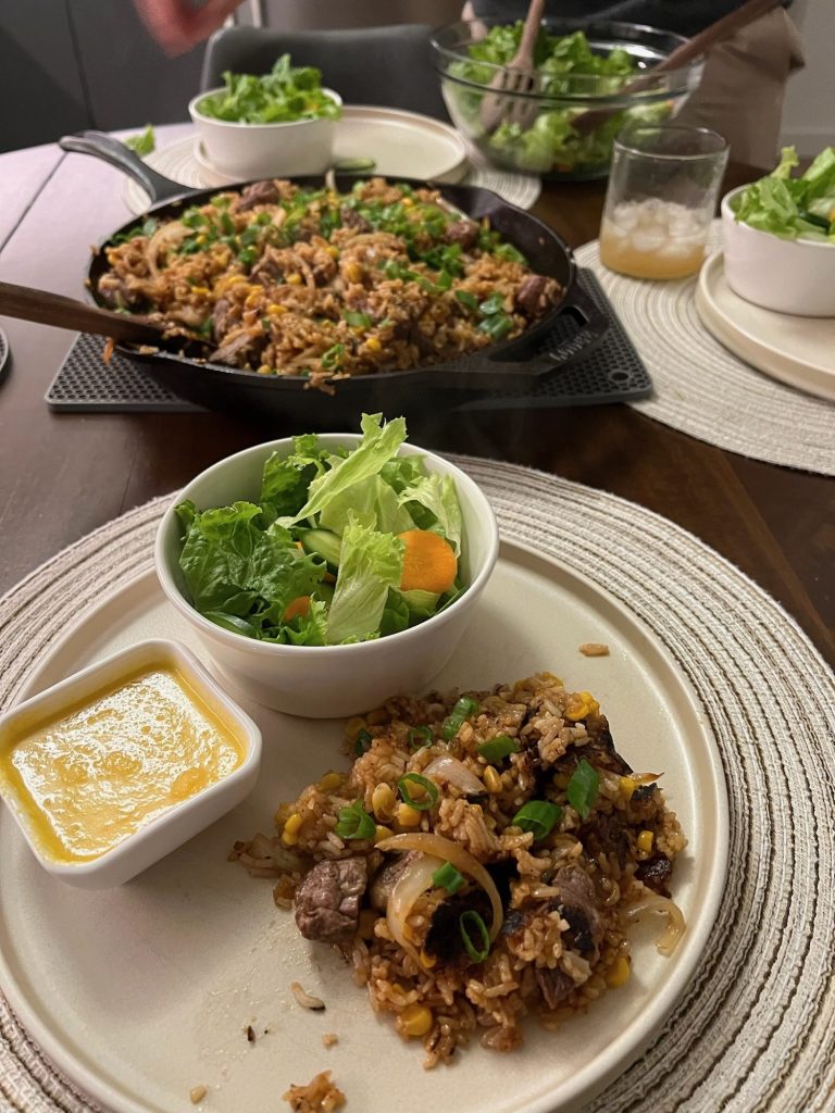 Plate with a side of ginger dressing, a small green salad and pepper beef rice