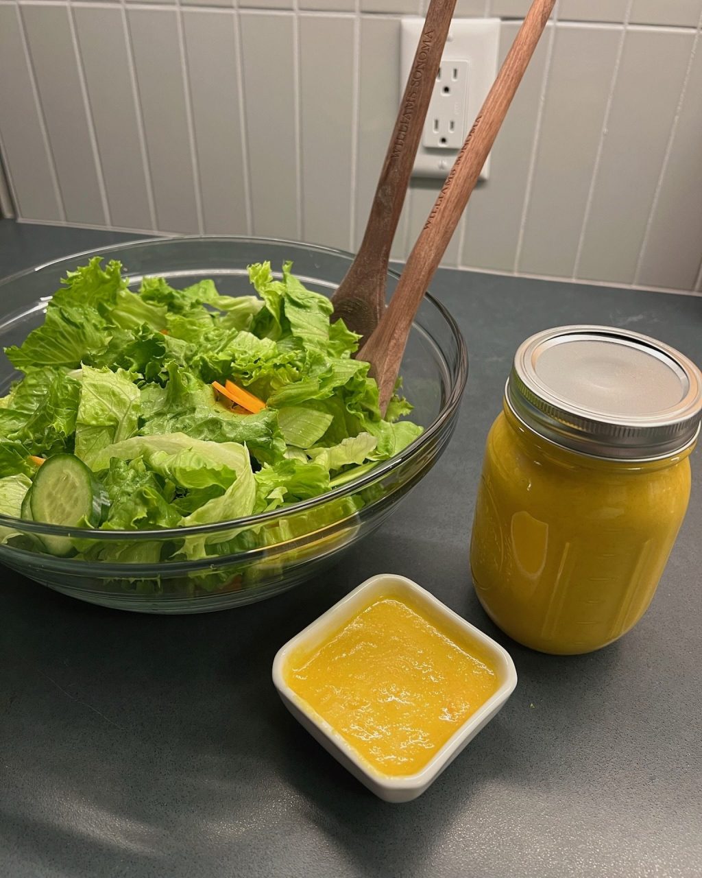 Bright orange ginger dressing in a small dish and a mason jar next to a bowl of green salad