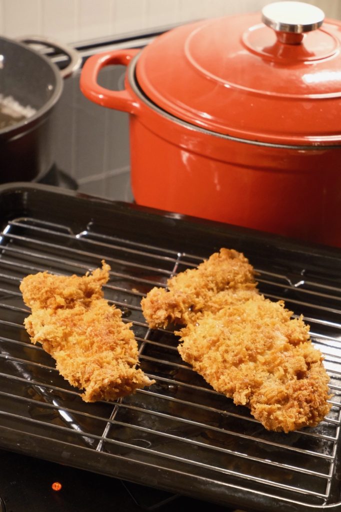 Two golden panko-fried chicken katsu cutlets draining on a wire rack beside the pot of curry