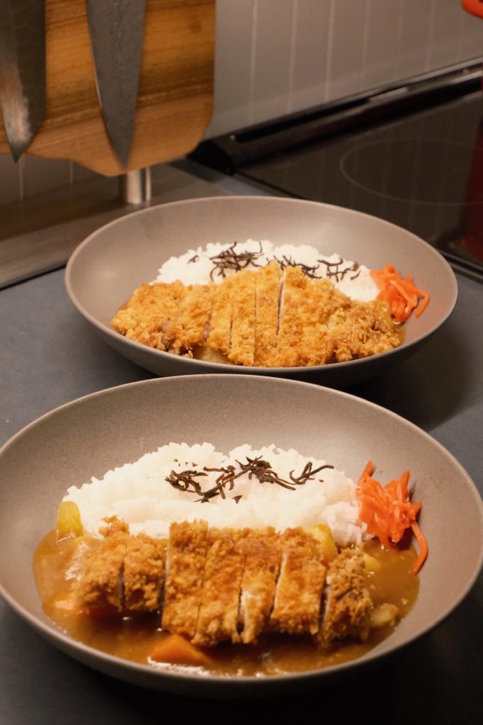 Two plates of katsu curry on the counter, each with sliced chicken katsu over curry and rice