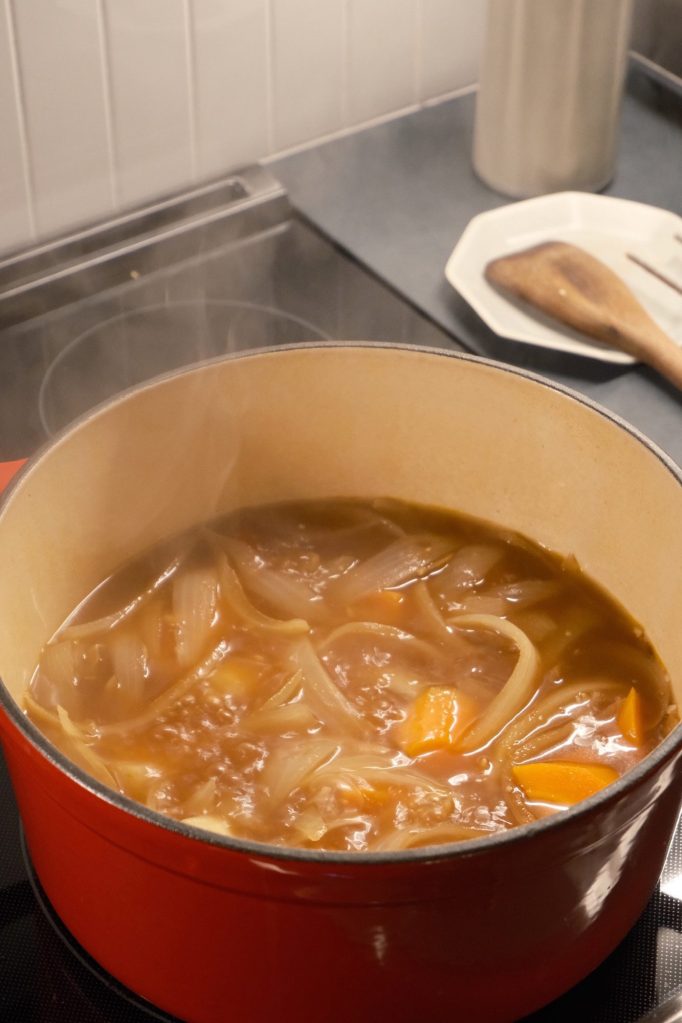 Japanese curry with onions, carrots and potatoes simmering in a red enameled pot on the stove