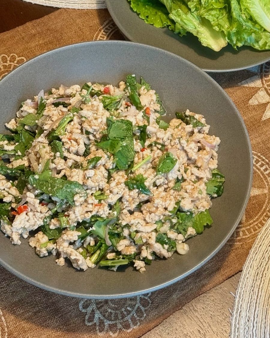 Thai laab with ground meat, mint, cilantro and chili in a gray bowl, with a plate of lettuce leaves behind