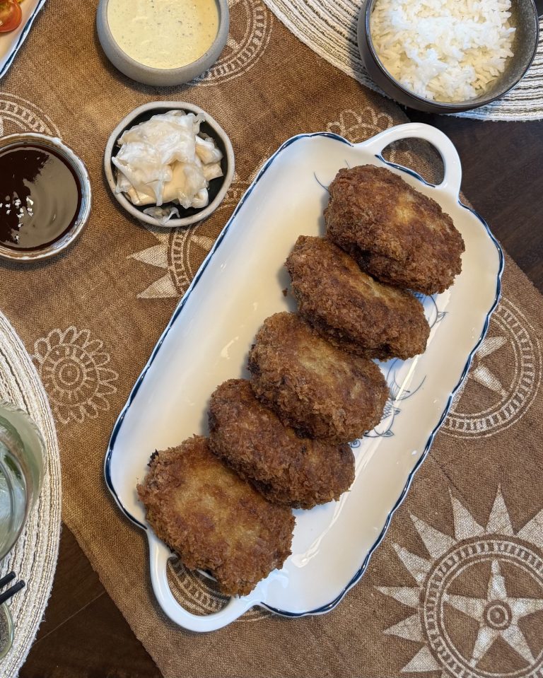 Overhead view of golden panko-crusted pork cutlets lined up on a white platter, with tonkatsu sauce, tartar sauce and rice on the table