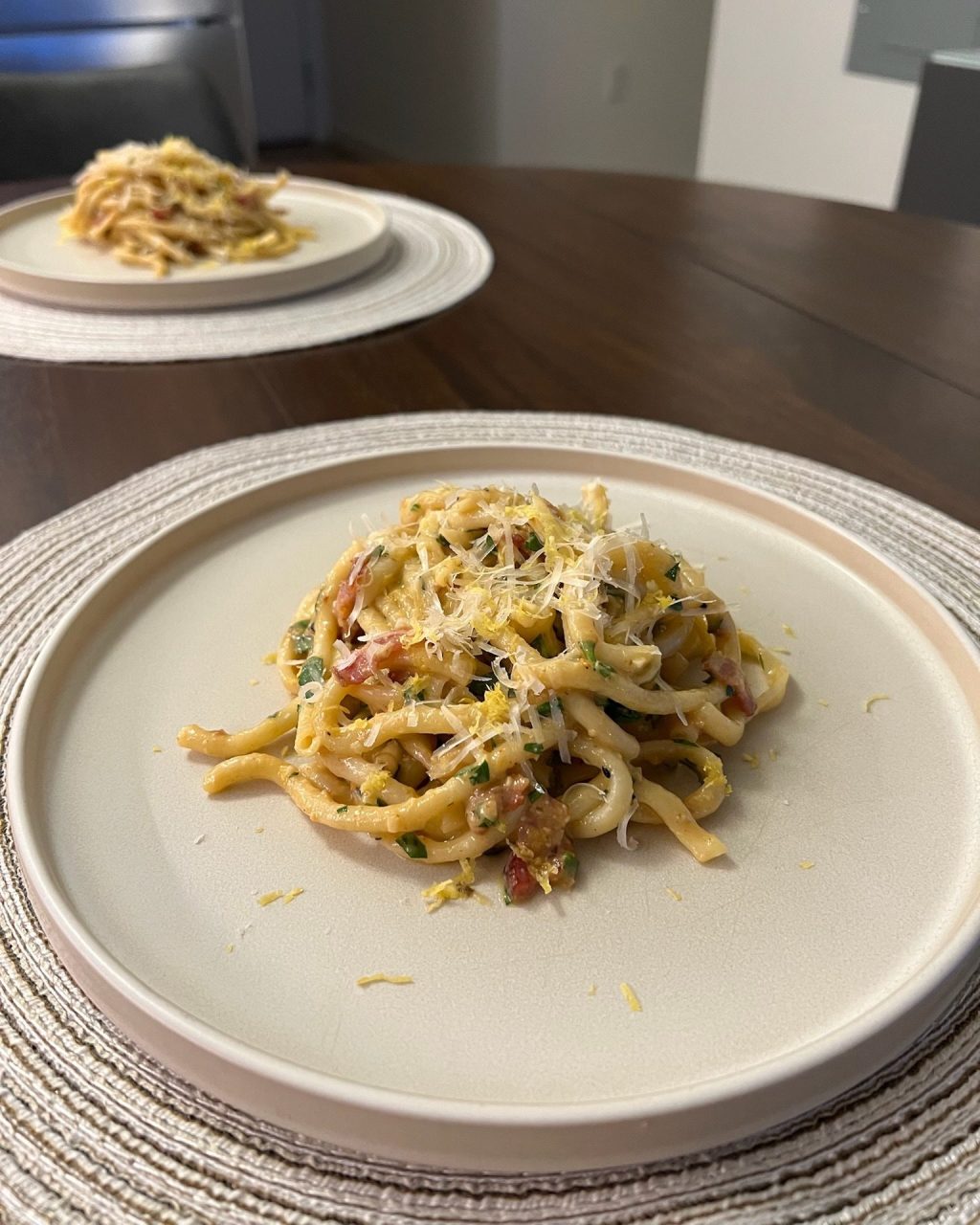 Plate of thick pasta in miso carbonara sauce with bacon, Parmesan, parsley and lemon zest
