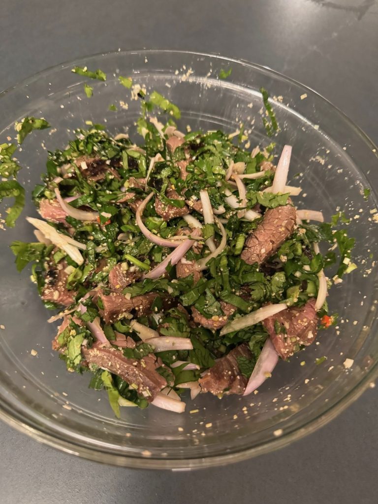 Glass bowl of sliced steak tossed with herbs, shallots and lemongrass
