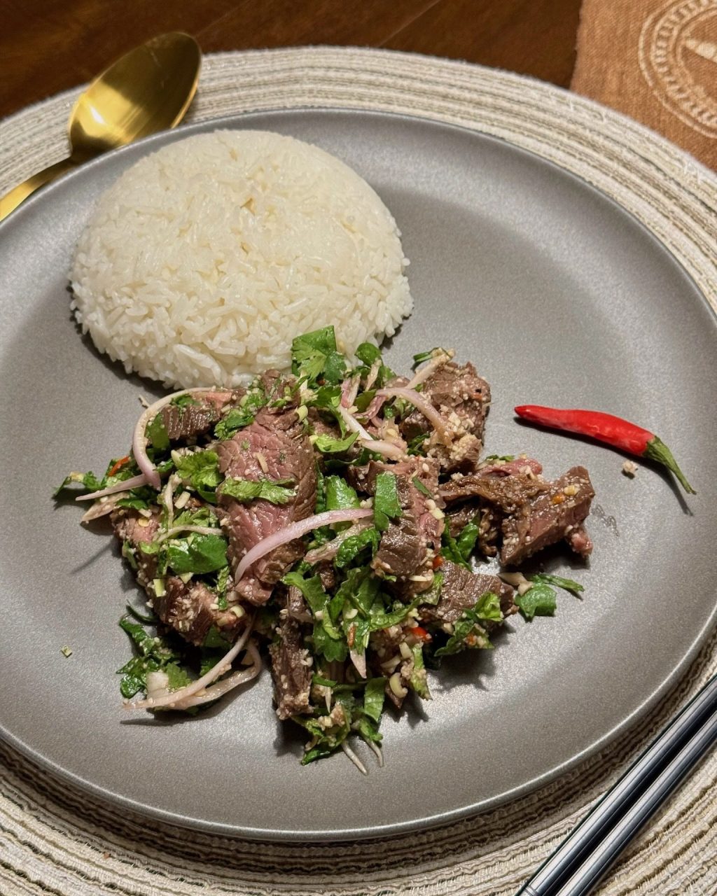 Thai grilled steak salad with mint, cilantro, shallots and toasted rice powder next to a dome of sticky rice and a red chili