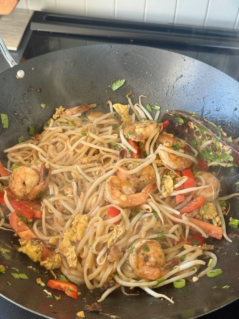 Rice noodles tossed with egg, bean sprouts and red pepper in a wok