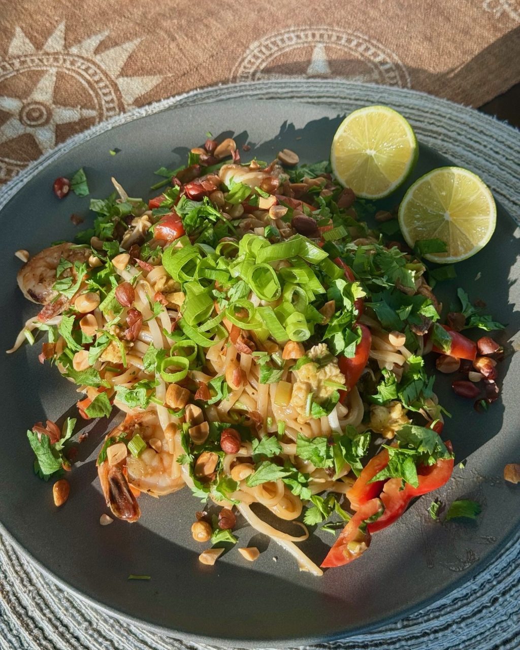 Plate of pad Thai topped with green onion, cilantro and crushed peanuts, with lime halves