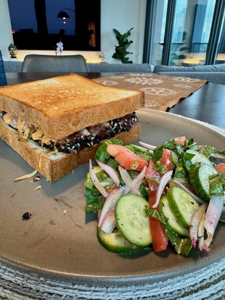 Seared ahi tuna sandwich on thick toasted milk bread next to a cucumber, tomato and onion salad