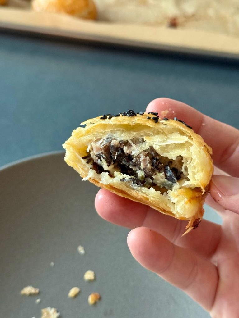 A hand holding a bitten pâté chaud showing flaky layers and the pork and wood ear mushroom filling inside