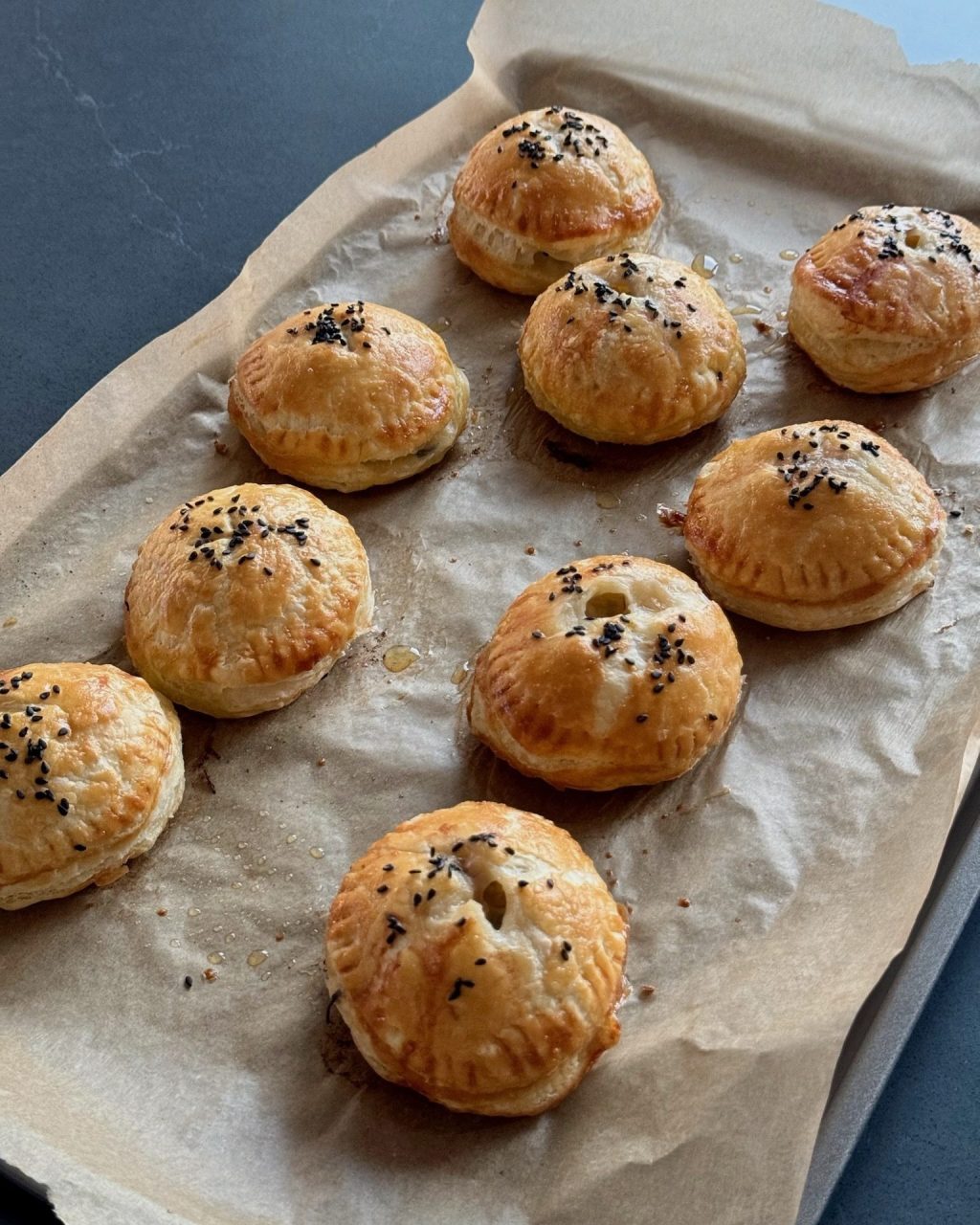 Golden baked pâté chaud puff pastries topped with black sesame seeds on a parchment-lined baking sheet