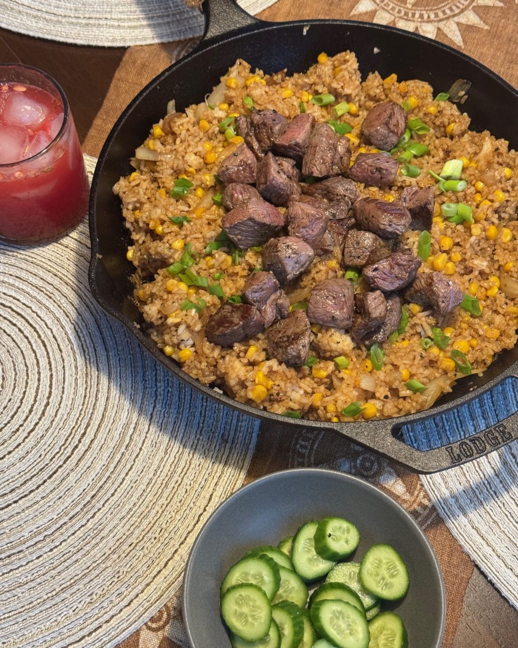 Cast iron skillet of pepper beef rice with seared steak cubes, corn and green onion