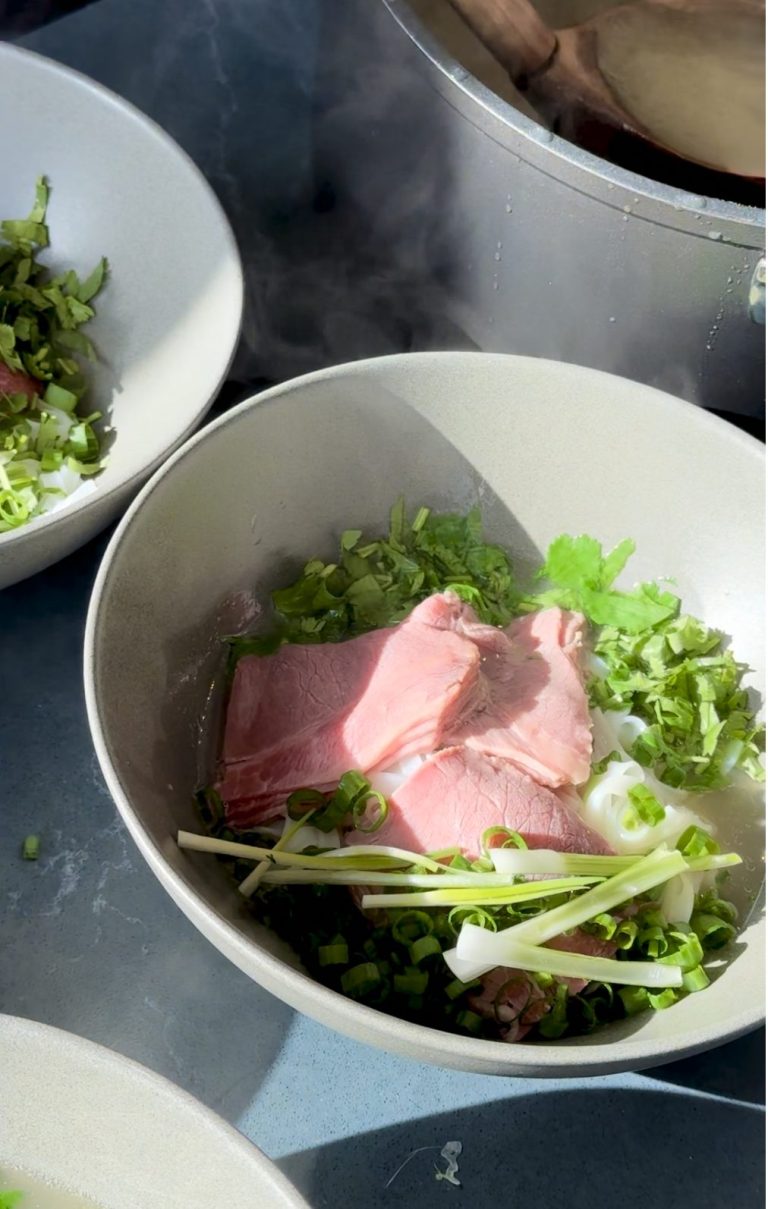 Thin slices of raw beef over rice noodles, green onions and cilantro, ready for hot broth