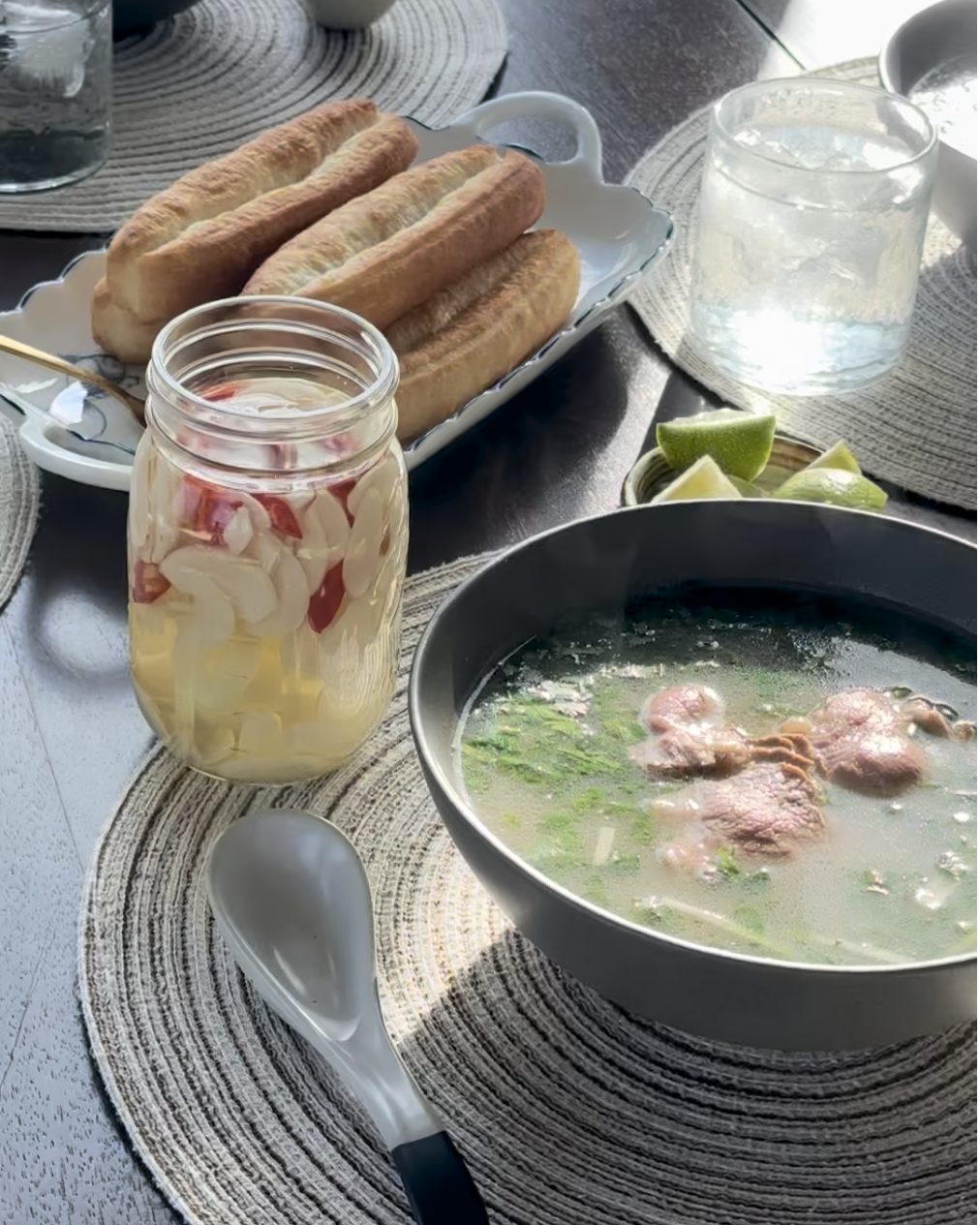 Bowl of clear beef pho with sliced beef and green onions, next to a jar of garlic vinegar and Chinese doughnuts