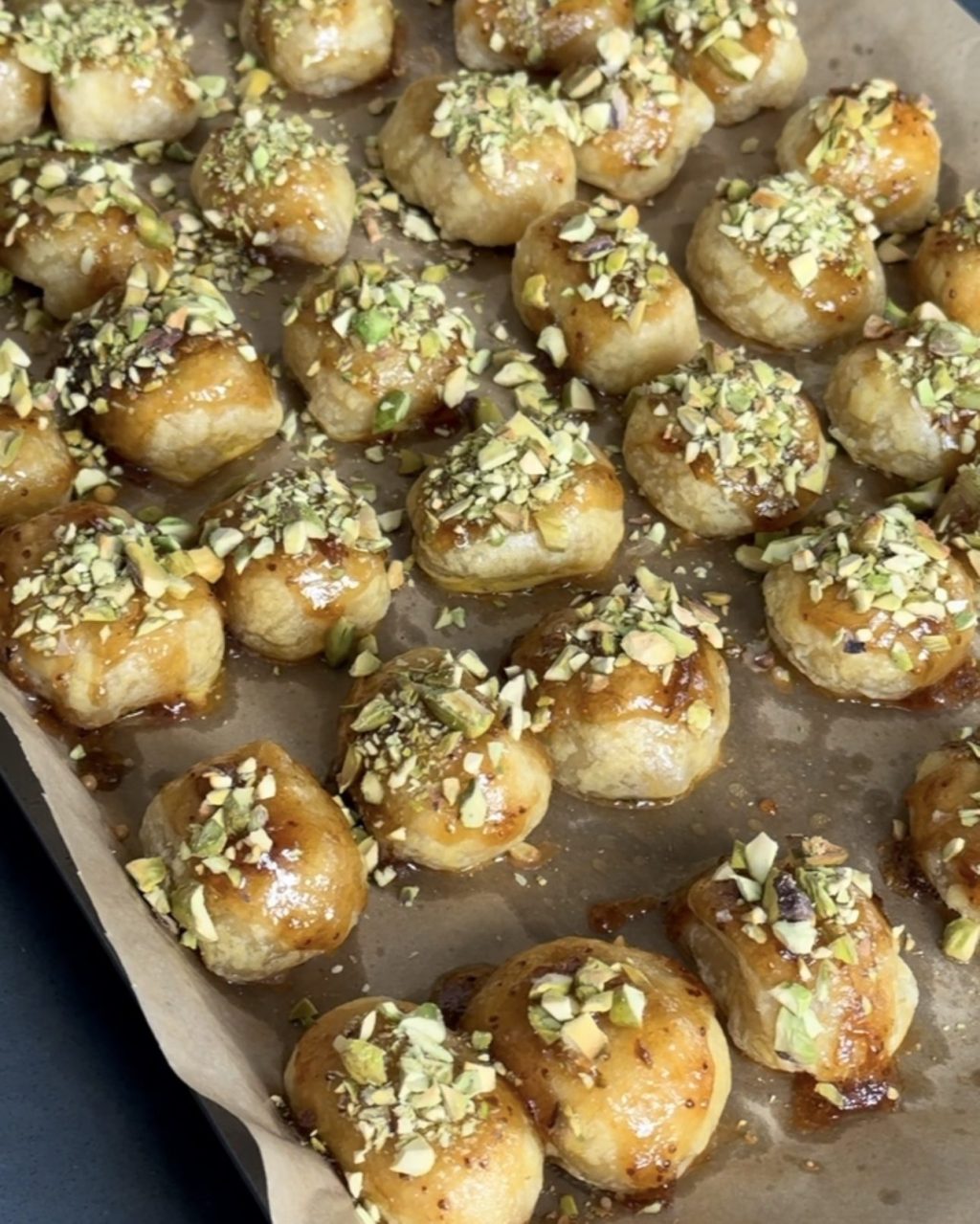 Golden puff pastry brie bites topped with chopped pistachios and fig honey glaze on a parchment-lined baking sheet