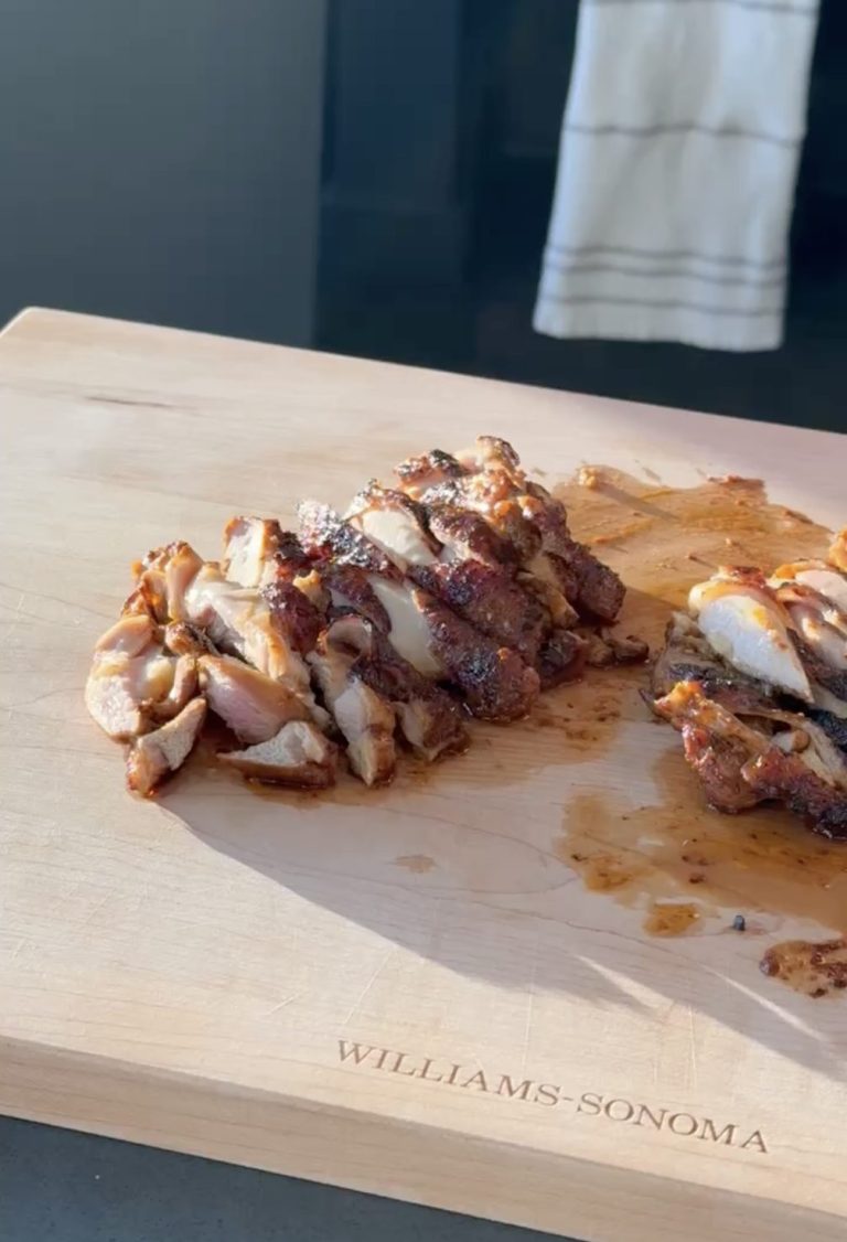 Charred marinated chicken thighs sliced on a wooden cutting board