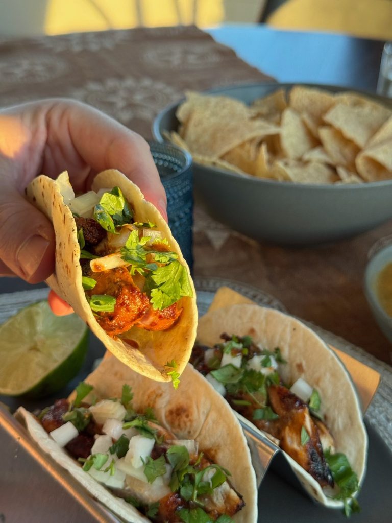Hand holding a pollo asado taco topped with diced onion and cilantro over more tacos and chips