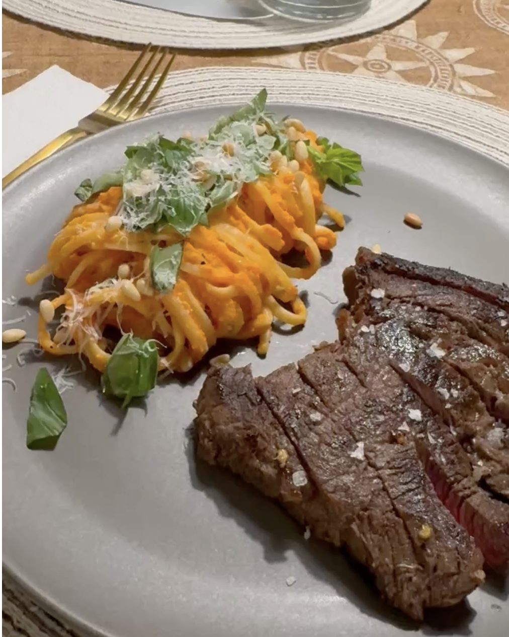 Twirl of pasta in roasted red pepper sauce topped with basil, Parmesan and pine nuts, served with sliced steak