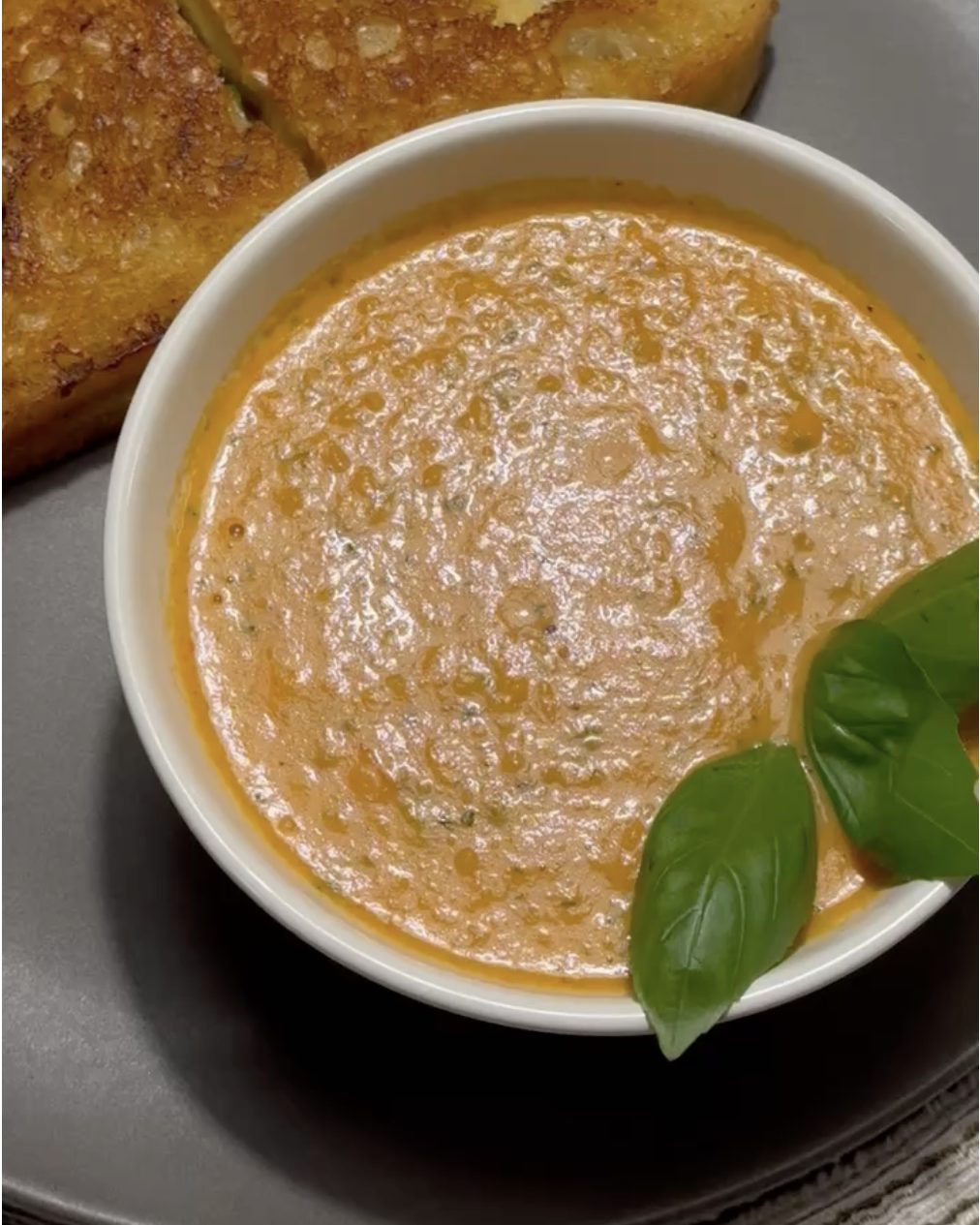 Bowl of creamy roasted tomato soup garnished with fresh basil, next to toasted bread