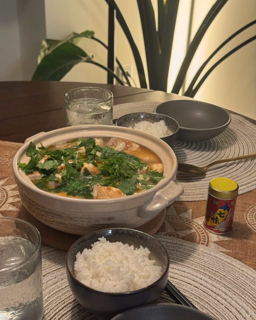 Donabe of salmon and daikon in miso broth topped with chopped cilantro, served with bowls of rice and shichimi togarashi