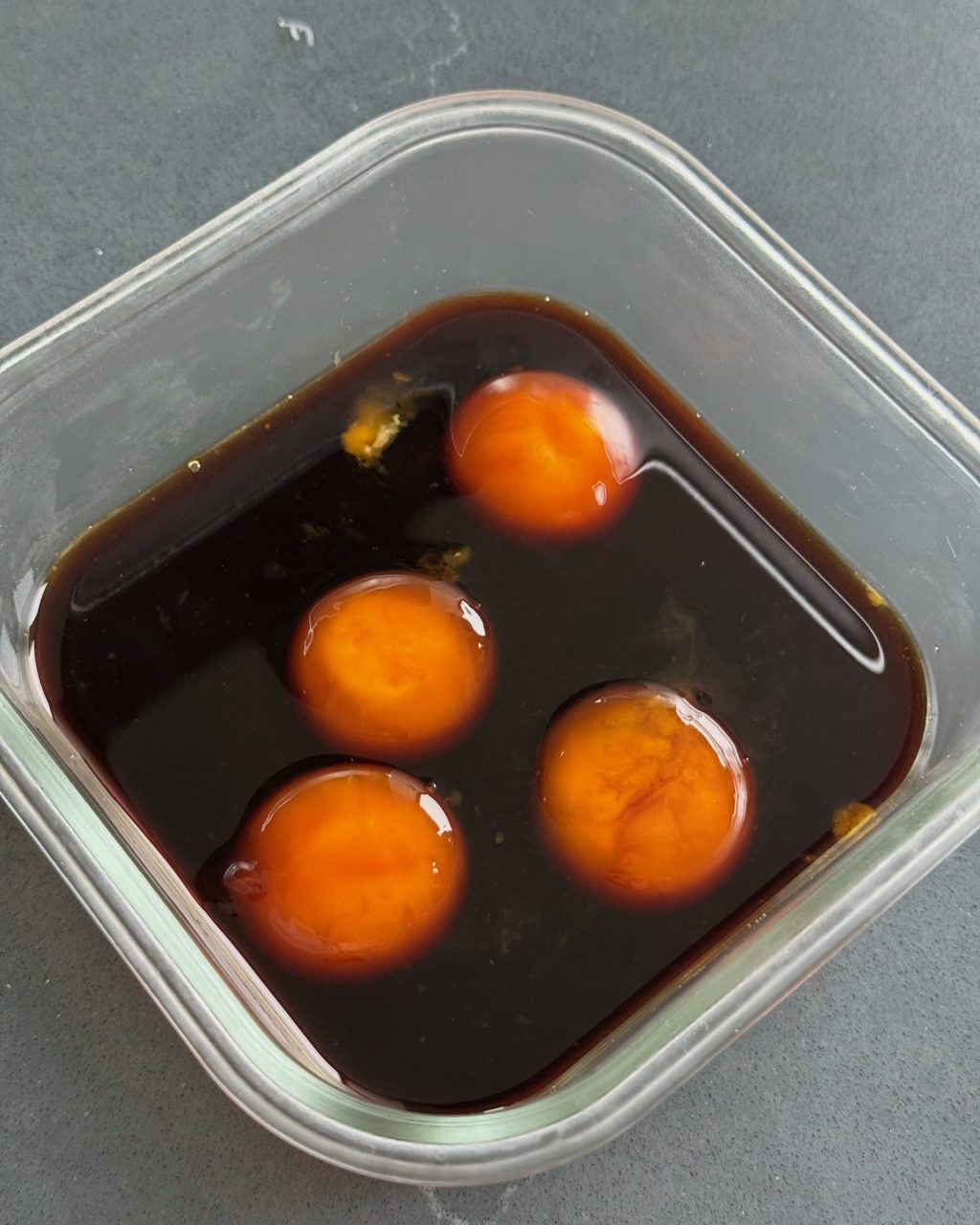 Egg yolks curing in a soy sauce brine in a glass container