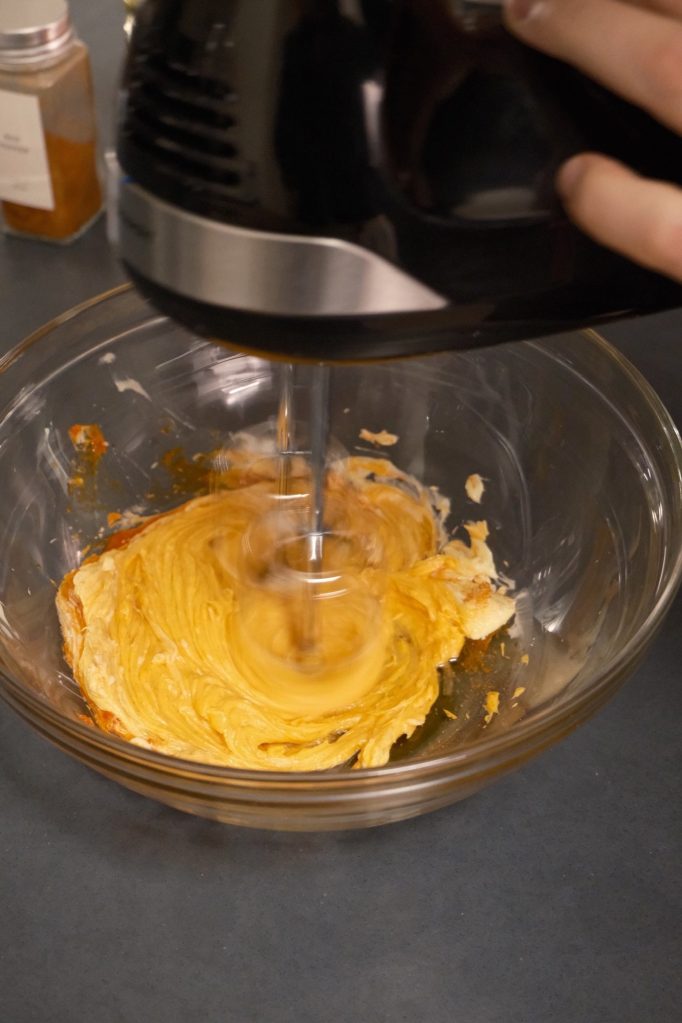 Hand mixer whipping butter and gochujang in a glass bowl