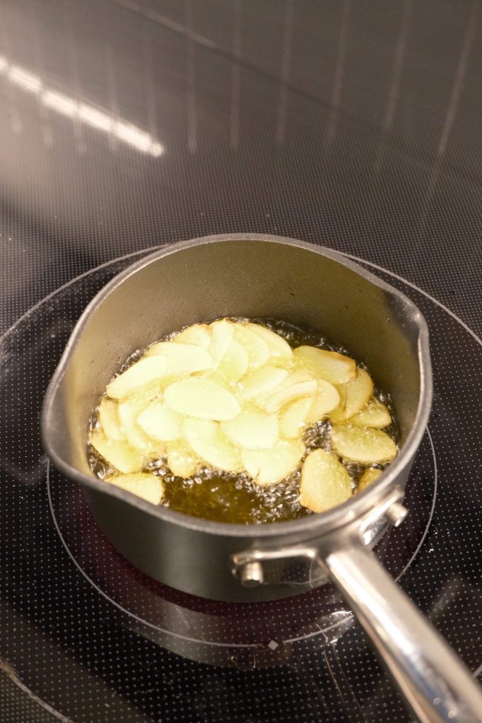 Thinly sliced garlic frying in oil in a small saucepan