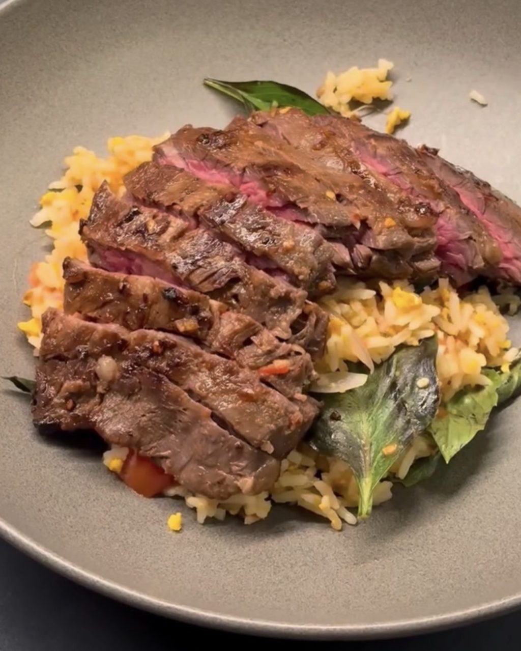 Sliced medium-rare skirt steak over Thai basil fried rice with tomato and fresh basil
